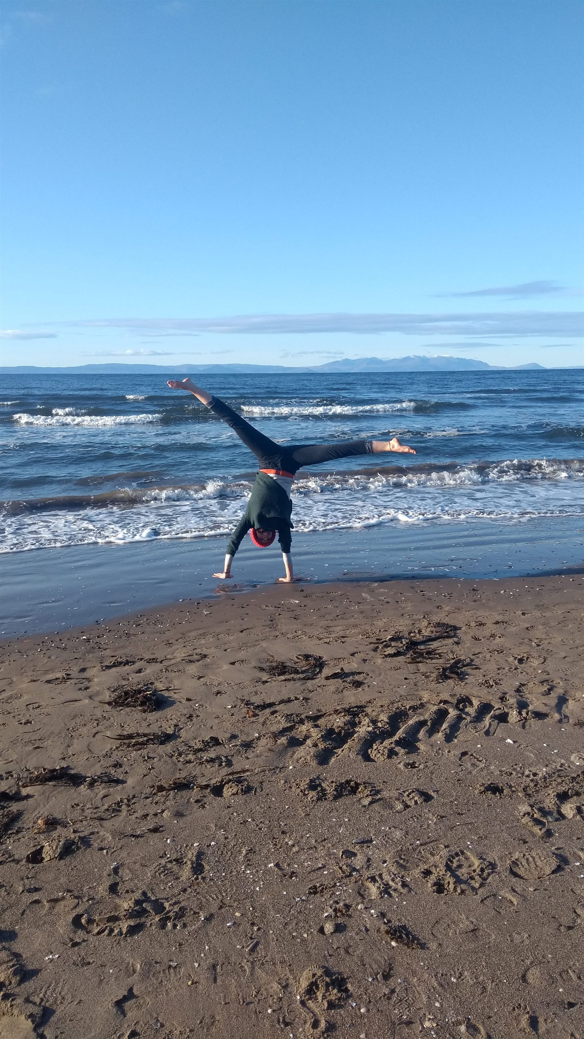 Christina Weis doing a handstand on a beach with the sea and mountains behind